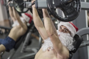 Genç fitness Noel Baba eğitimi alıyor. Noel arifesinde ağırlık kaldırıyor.