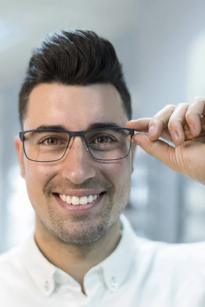 Bello uomo cercando su occhiali in ottico occhio negozio — Foto Stock