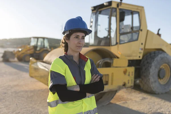 Worker woman posing near to construction vehicle