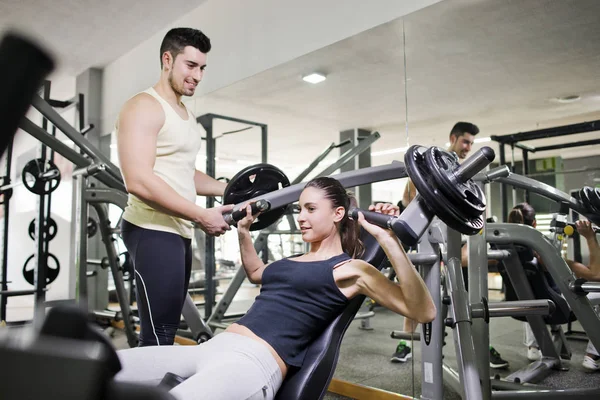 Gym coach helping girl doing pectoral exercises with ambient lightning