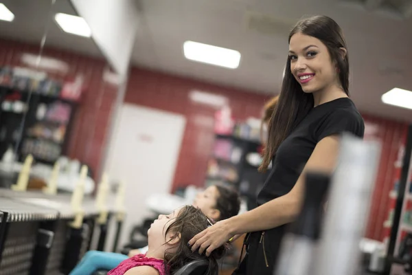 Hairdressers with little girls in beauty center saloon, woman looking at camera and smile