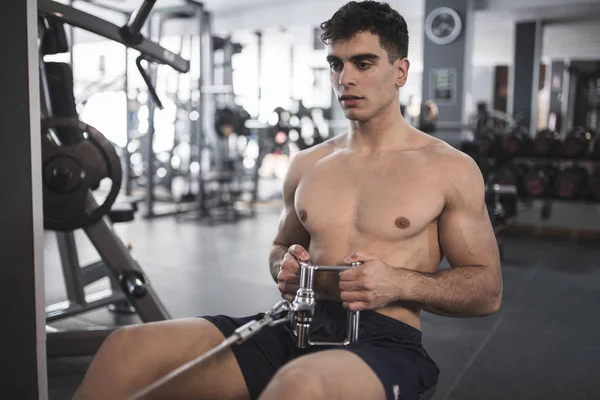 Rowing young man in gym training shirtless
