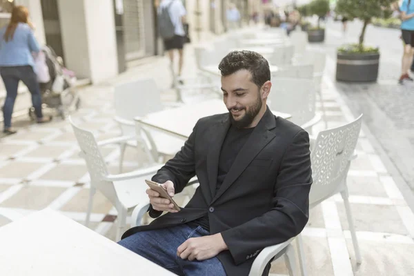Bearded suit man in bar terrace looking smartphone and smiling
