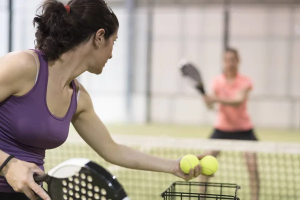 Woman serving balls to other in paddle tennis class