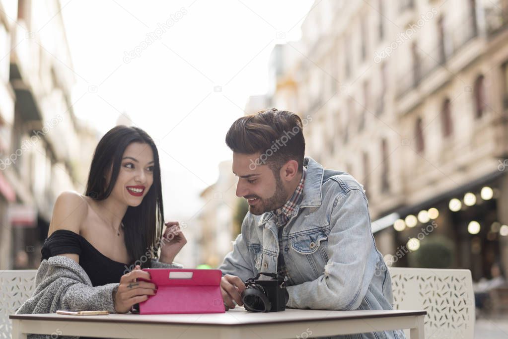 Young couple reviews photography in digital tablet  while waiting drinks in bar terrace in city outdoors image
