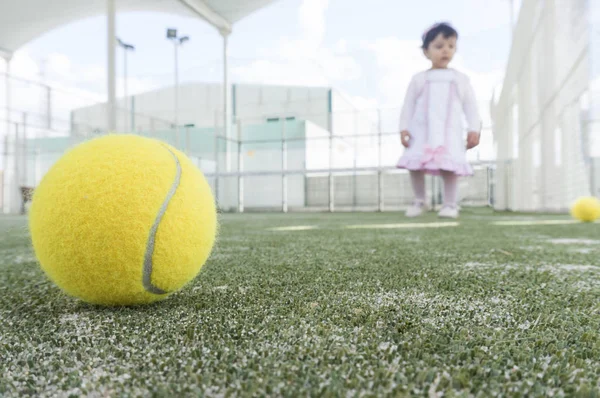 Baby in paddle tennis court learning how to play and collecting balls