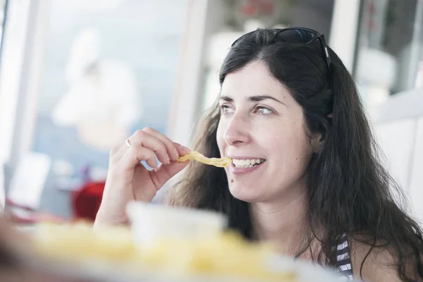 Mooie brunette vrouw eten chips in restaurant — Stockfoto