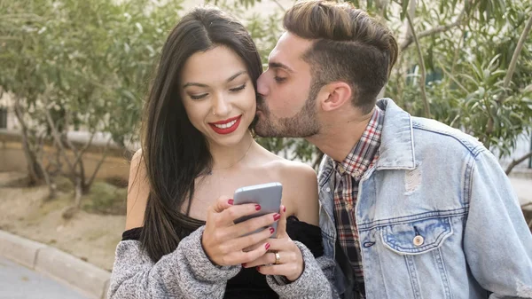 Mann Küsst Junge Frau Während Sie Smartphone Benutzt — Stockfoto