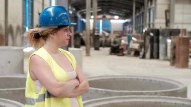 Kasklı kadın fabrika işçisi kameraya gülümsüyor ve başparmağını kaldırıyor.