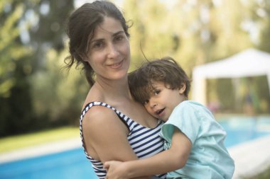 Anne ve oğul bahçede kucaklaşıyor, çocuğa odaklanıyor.