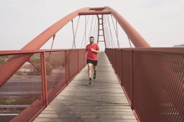 Kızıl yaya köprüsünde koşan sakallı adam.