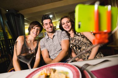 Lokantada elinde alkol bardakları olan üç arkadaş telefon ve sopayla kendilerini alıyorlar.