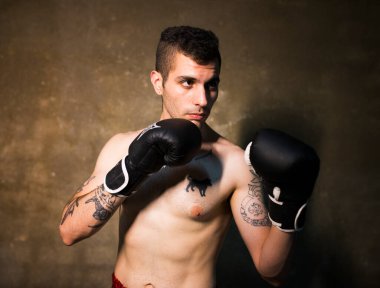 Stüdyoda poz veren Muai Thai elbiseli ve dövmeli genç bir adam.