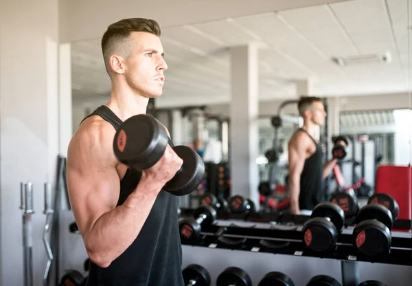 Beden eğitiminde adam aynanın yanında kaslarını çalıştırıyor.