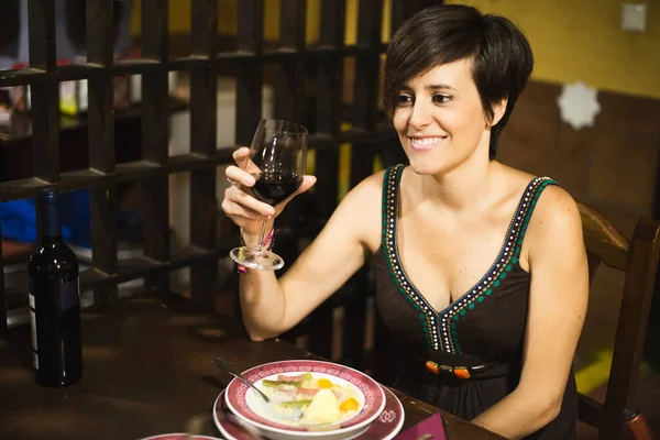 Woman eating spanish stew dish and wine in bar in bar and smiling