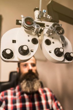 Fotopter optik mağazadaki sakallı adamın vizyonunu ölçmeye hazırlanıyor.