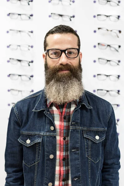 Bearded cool man tries on glasses in optical store