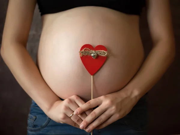 Pregnant woman. Belly pregnancy. Red heart on the background of the abdomen. 9 months of pregnancy.