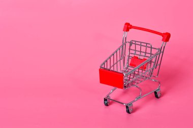 Pembe arka planda küçük bir alışveriş arabası. Tüketici sepeti. Mağazada alışveriş.