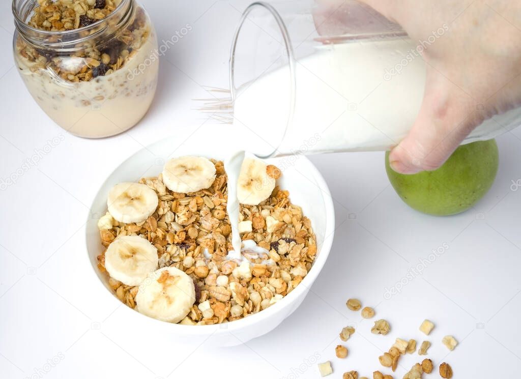 Milk splashing in a bowl of fresh granola with a mixture of wheat, oats and bran with dried fruits and nuts on a white background.