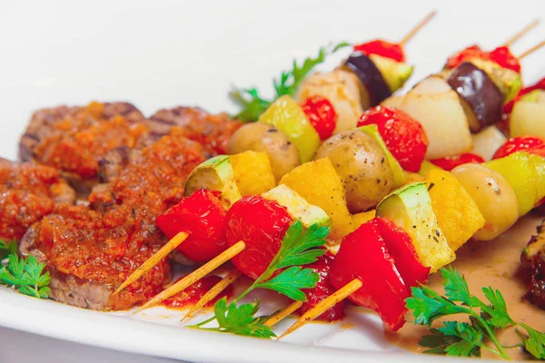 Vegetable skewers with meat on a white plate. Baked vegetables on shashkah with beef. Grilled meat on a barbecue with vegetables