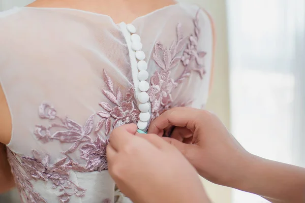 Putting on the bride\'s dress. Morning of the bride. The back of the wedding dress. Buttons on the back of the dress. Corset and lacing of the wedding dress. Pink beautiful lace on the dress.