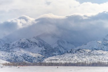 Kış dağlar. Kar dağların kaplı. Kış manzarası. Eteklerinde kışın güneşli bir günde. Bulutlar üzerinde karlı dağlar.