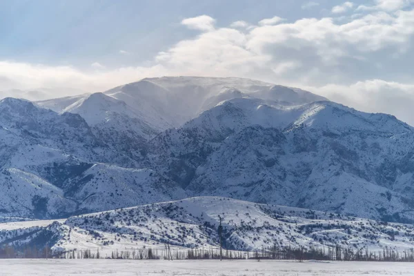 Winter mountains. Snow covered mountains. Winter landscape. Sunny day in the winter in the foothills. Clouds over snowy mountains.