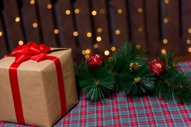Işıklar arka plan üzerinde Noel hediyesi. Kraft kağıt yeni yıl arka plan üzerinde hediyeler ile kutu. Bokeh çelenk Noel çam dalı ile Noel hediyeleri arka planı. Kraft kağıt bir kırmızı yay ile kare hediye kutusunda.