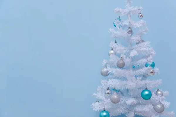 White Christmas tree on a blue background. Christmas decoration. White artificial Christmas tree with blue and silver balls. New year background.