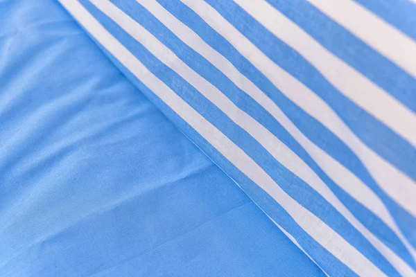 Pamuk yataklar. Beyaz-mavi çizgili yastıklar. Kumaş dokusu. Yastık ve battaniye yatağa vardır. Yatak odası tekstili kümesi. Güzel ve kaliteli çarşaflar. battaniye ve yastık yatak.