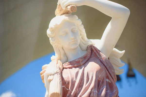 The statue of the Greek goddess. Portrait of a statue of a woman against the sky. Sculpture of an adult woman with curly hair. Cultural object in the park. Marble wares