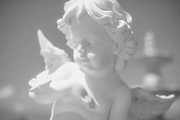 Angel Statue. Portrait of an Angel against the sky. Sculpture of a little boy with curly hair. Cultural object in the park. Marble wares