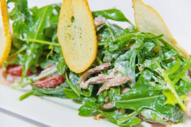 Bir sunucu plaka üzerinde yeşil salata. Dekor plaka pembe suyu. roka kruton ve kiraz domates salatası. gıda et ve krema sos ile. Beyaz tabak.