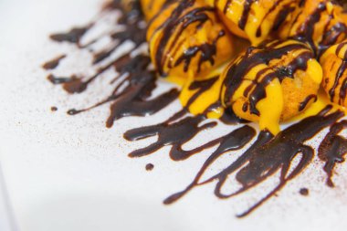 Çikolata soslu profiterol. Beyaz tabakta tereyağı krema ile Mini kek. Profiterol ve nane yaprakları ile süslenmiş çikolata ile yemek. Lezzetli tatlı tatlı. Yararlı tatlılar taze yemek.