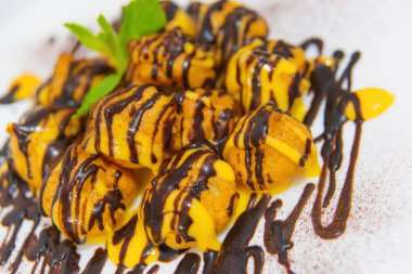 Çikolata soslu profiterol. Beyaz tabakta tereyağı krema ile Mini kek. Profiterol ve nane yaprakları ile süslenmiş çikolata ile yemek. Lezzetli tatlı tatlı. Yararlı tatlılar taze yemek.