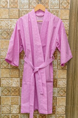 Color cotton bathrobes for the hotel. Pink and white bathrobes with a circle pattern. Light summer dressing gowns with a belt. Bathrobe hanging on a hanger. Home textiles in the interior. clipart