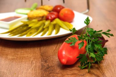 Bir tabakta sebze taze ve turşu. Tuzlu salatalık ve domates plakaları. Kırmızı ve beyaz soslu biftek. Soğan, sarımsak, domates, domates, Bulgar biber, maydanoz. Ahşap bir masa üzerinde taze yiyecek.