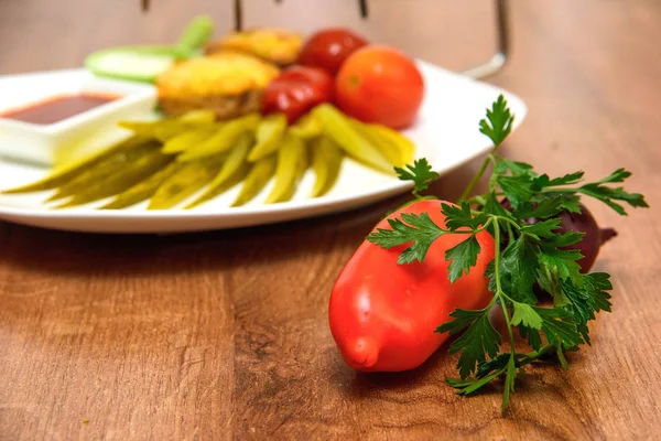 Bir tabakta sebze taze ve turşu. Tuzlu salatalık ve domates plakaları. Kırmızı ve beyaz soslu biftek. Soğan, sarımsak, domates, domates, Bulgar biber, maydanoz. Ahşap bir masa üzerinde taze yiyecek.