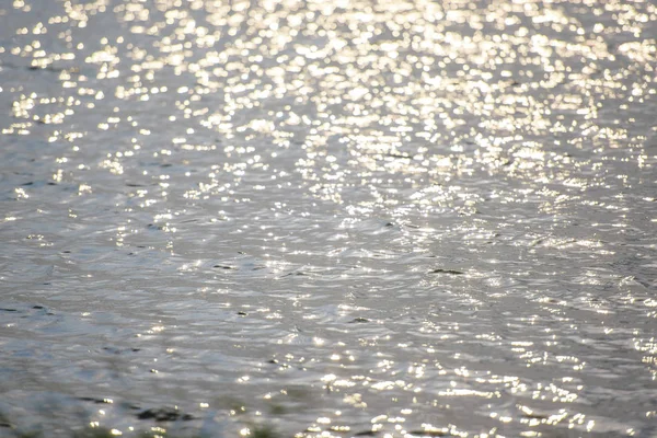 Water ripples. The glimmer of light on water. Silver gray and blue water with the reflection of the sun\'s rays. Photophone blue with white circles. Reflection of radiance on the water. Water surface and waves.