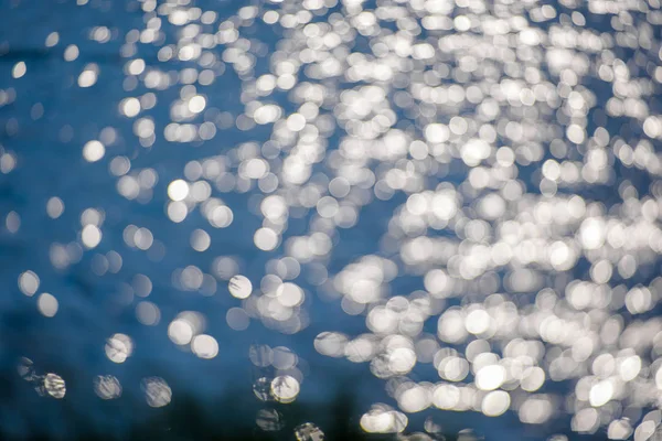 Water ripples. The glimmer of light on water. Silver gray and blue water with the reflection of the sun\'s rays. Photophone blue with white circles. Reflection of radiance on the water. Water surface and waves.