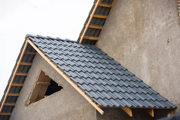 Building a house with a tiled roof. Directing wooden roof beams. Gray roof tiles and chimney of red brick. Unfinished house. Attic under the roof of the house. Round roof slope.