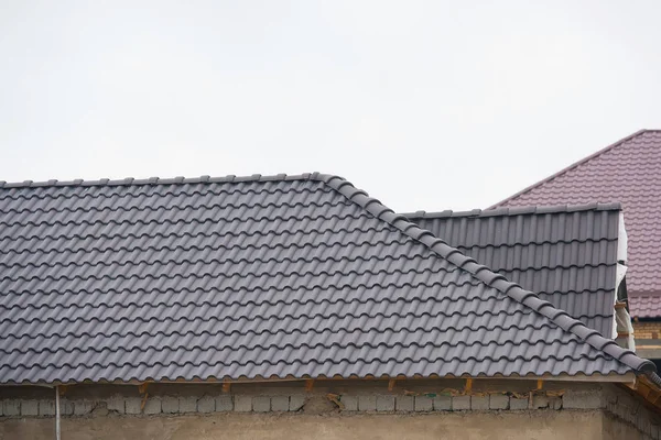 Building a house with a tiled roof. Directing wooden roof beams. Gray roof tiles and chimney of red brick. Unfinished house. Attic under the roof of the house. Round roof slope.