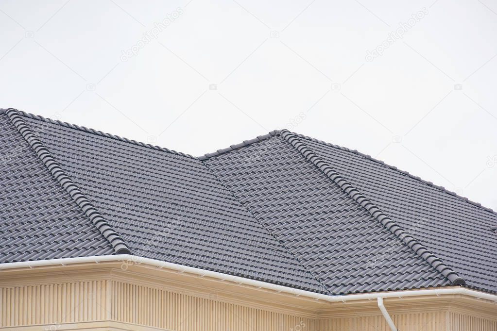 Building a house with a tiled roof. Directing wooden roof beams. Gray roof tiles and chimney of red brick. Unfinished house. Attic under the roof of the house. Round roof slope.