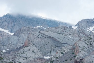 Yüksek dağlar. Bulutlu gökyüzü. Karla kaplı dağ yamaçlarında. Dağ silsilesi. Engebeli arazi. Karlı zirveleri. Dağlarda bitkiler.