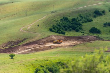 Engebeli yüzey. Traktör yere kazıyor. Bitki örtüsü dağ yamaçlarında. Kuş bakışı. Engebeli arazi. Arazi kazdık.