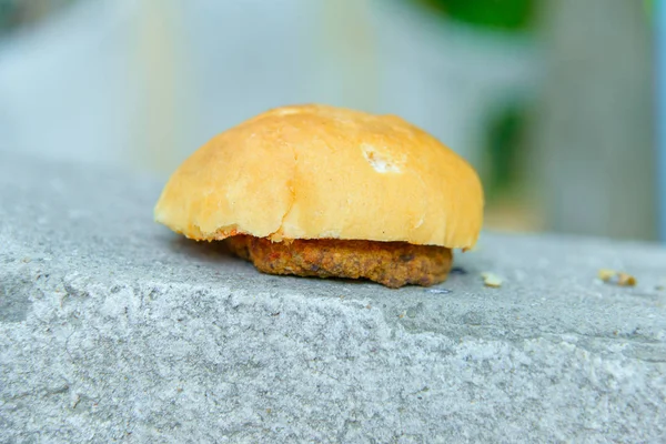 Hamburger on concrete. Half a cheeseburger on a granite slab. Dropped the bun and cutlet on the floor. Delicious lunch on gray granite.