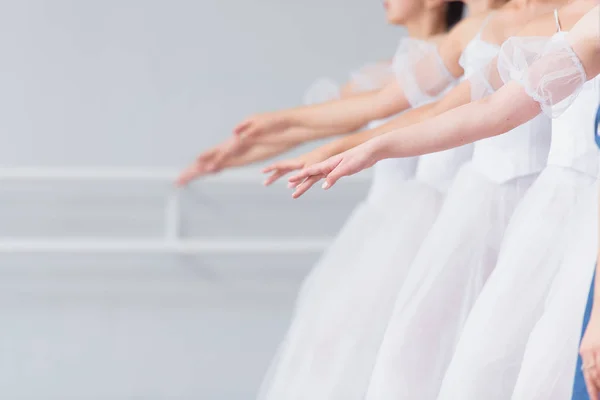 Exercises in the ballet school. Ballet classes. A group of girls standing in a row, stretched out their arms. Children in white dresses for dancing. Rukapa raised in line, brush slightly down.