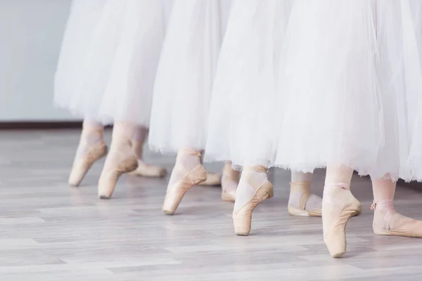 Feet in pointe. Exercises in the ballet school. Ballet classes. A group of girls standing in a row, stretched out their legs, shod in pointe. Children in white skirts. The teacher leads a dance lesson.