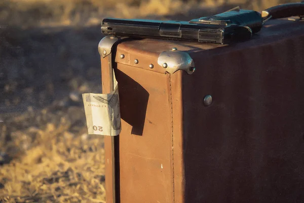 Old leather brown suitcase. Vintage. One dollar bill sticks out of a suitcase. Pistol lying on a suitcase. Guitar case and suitcase are in the trunk of the car.